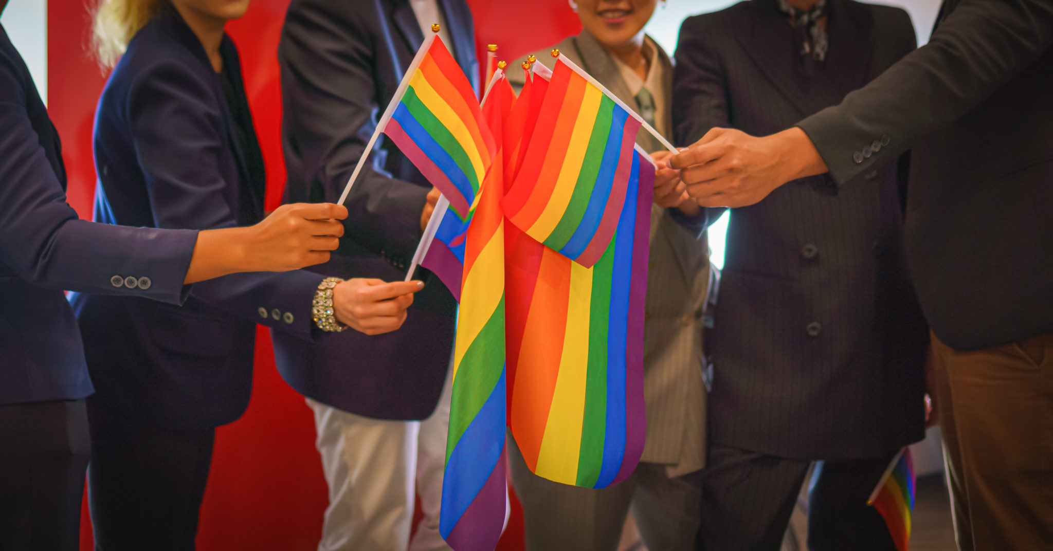 diverse group of business people (man, woman, gay, transgender, lesbian, asian, caucasian, african american, lgbtq) with rainbow flag on hand combine together as teamwork in office, selective focused